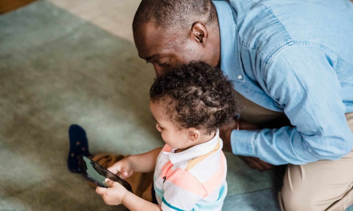 Adulto brinca com criança pequena, que tem celular nas mãos; imagem meramente ilustrativa -  (crédito: George Pak/Pexels)
