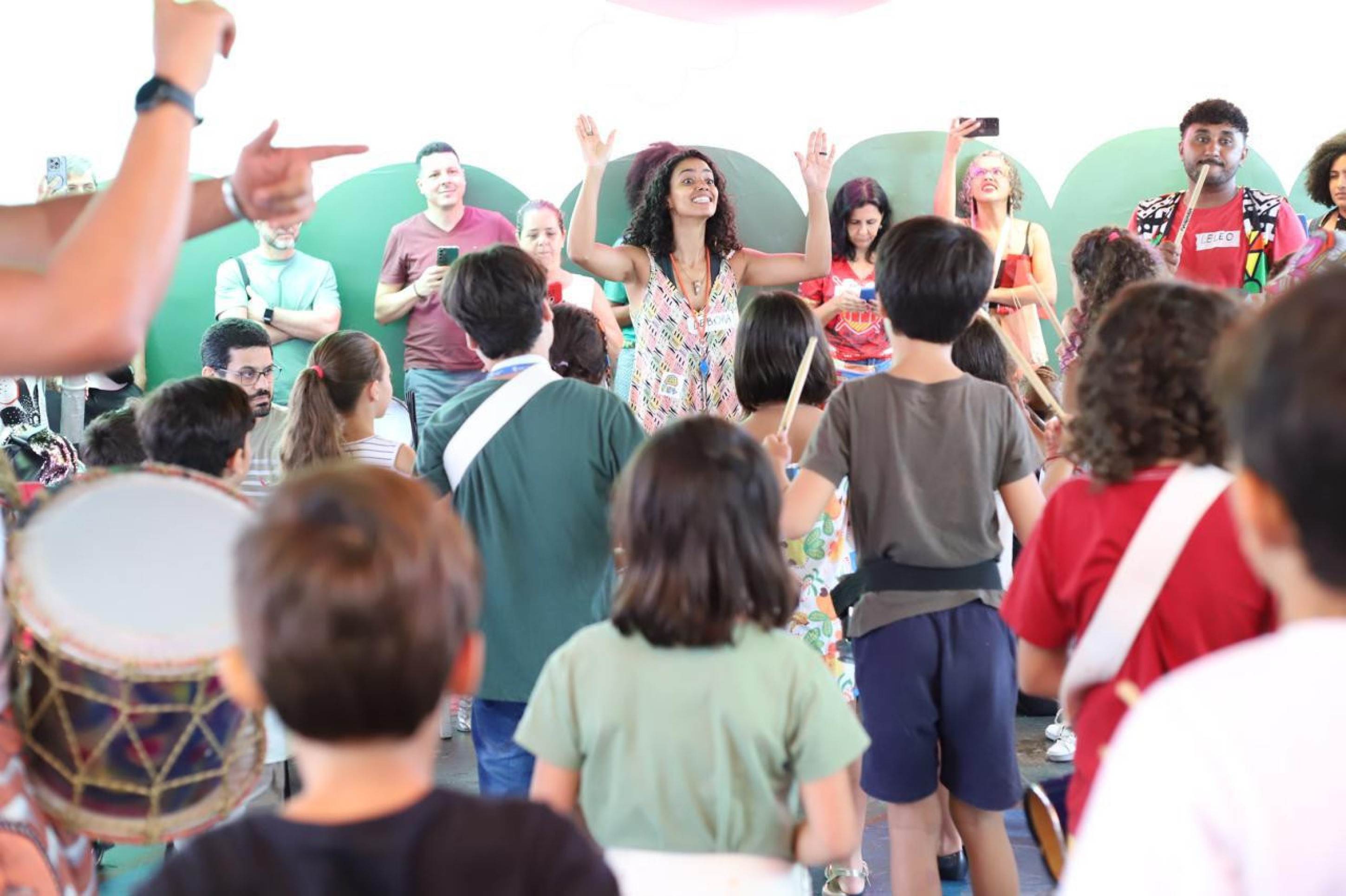 Meninos e meninas do Bloco das Crianças, de BH, segura tambores e tem aula de percussão, orientados por professora que tem os braços para o alto