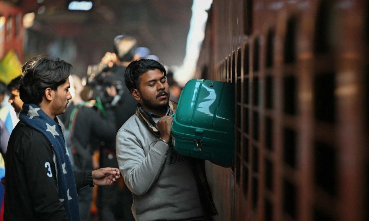 Passageiros retiram bagagens da janela de saída de emergência de um vagão de trem na estação ferroviária em Nova Delhi, na Índia  -  (crédito: Sajjad HUSSAIN / AFP)
