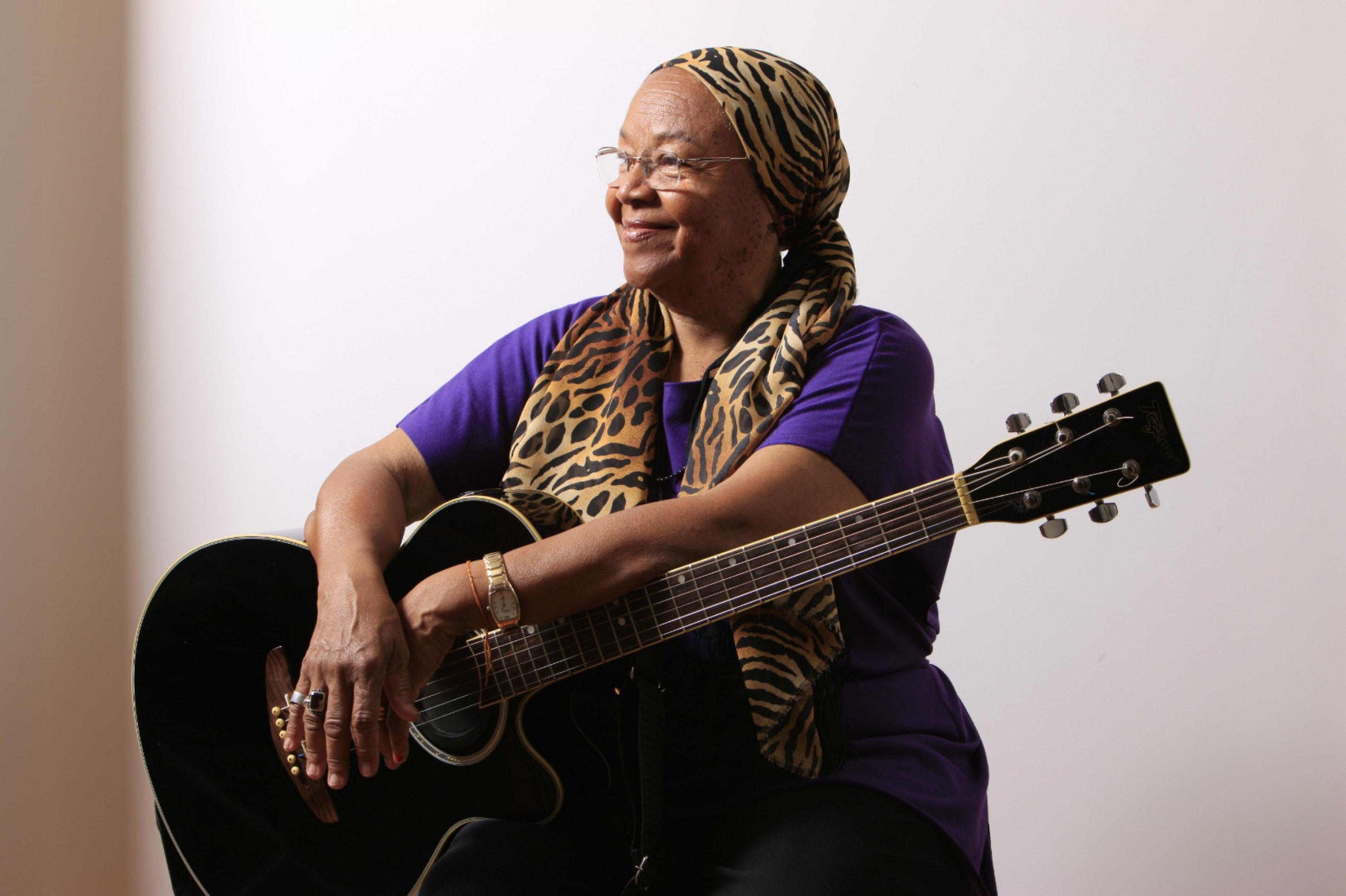 Cantora Dona Jandira sorri e segura o violão em foto feita por Daniel Mansur