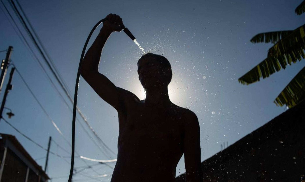 Um homem se refresca com uma mangueira na rua durante a onda de calor no bairro de Guaratiba, no Rio de Janeiro -  (crédito: TERCIO TEIXEIRA / AFP)