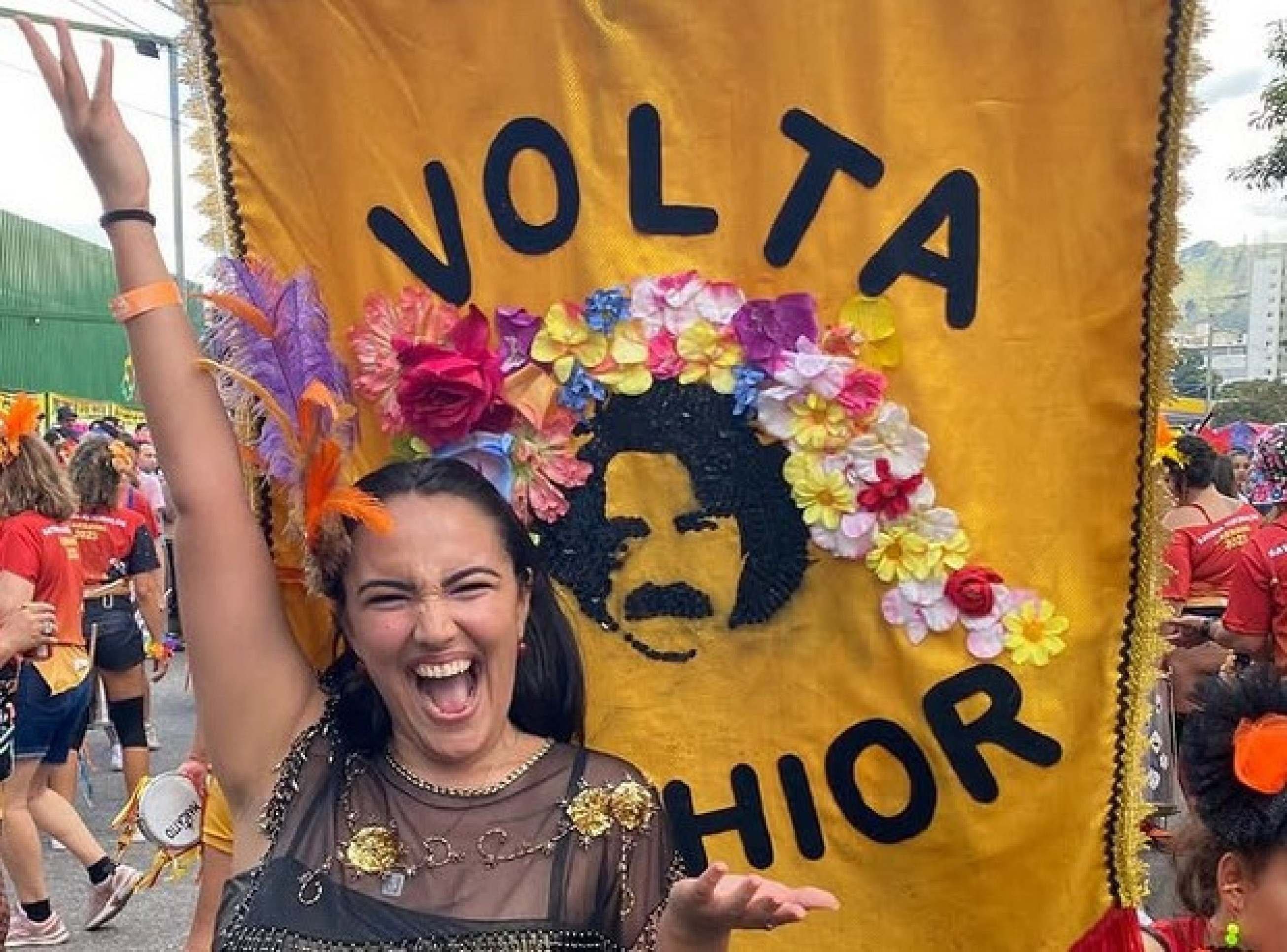Vannick, filha de Belchior, sorri diante do estandarte do bloco mineiro Volta Belchior