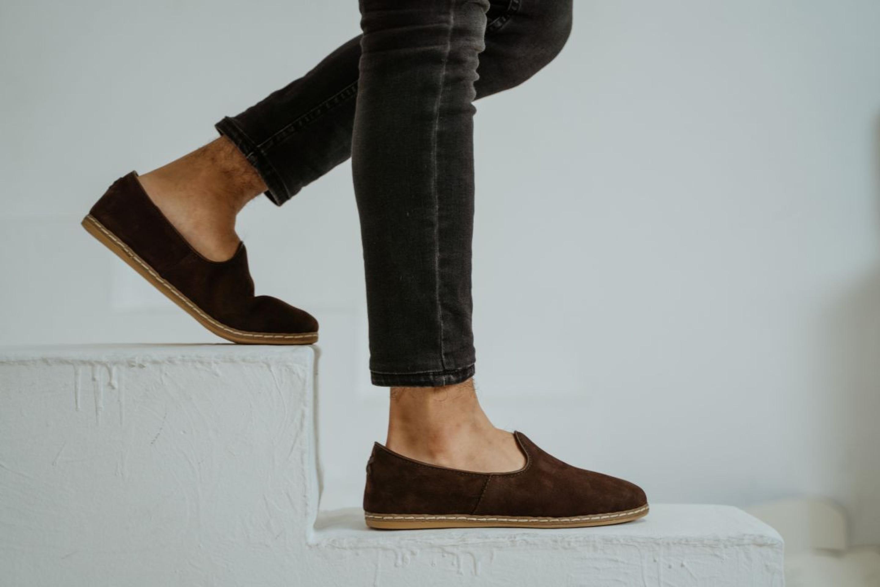 Lembre-se de sempre usar produtos adequados, evitar molhar o material em excesso e armazená-los corretamente Pessoa descendo a escada com tênis de camurça e calça jeans