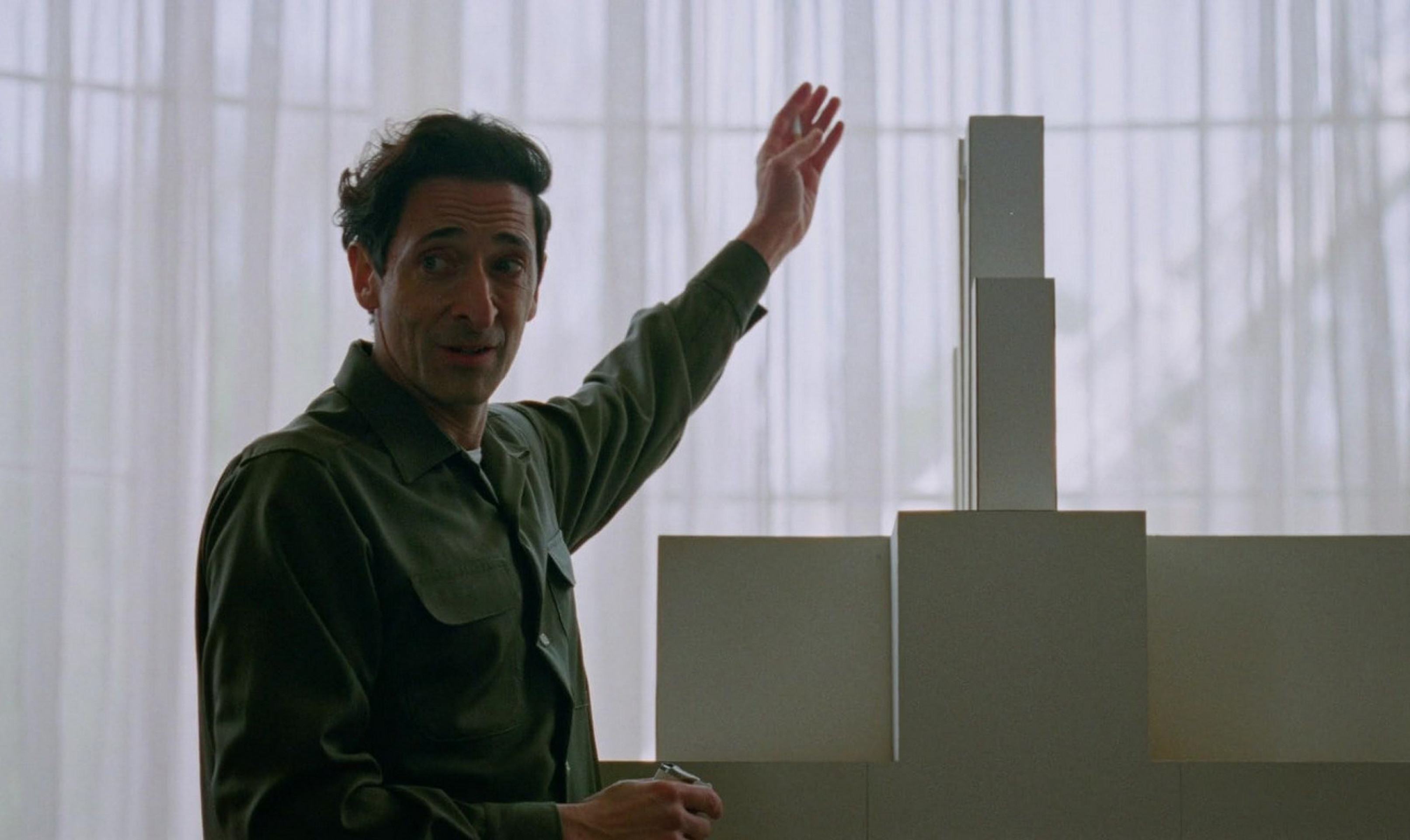 Adrien Brody como o arquiteto húngaro Lázló Toth, protagonista do filme 'O brutalista' e forte candidato ao Oscar de Melhor Ator, que será entregue no domingo (2/3) Ator Adrien Brody está de lado, em frente a maquete com formas modernistas em cena do filme O brutalista