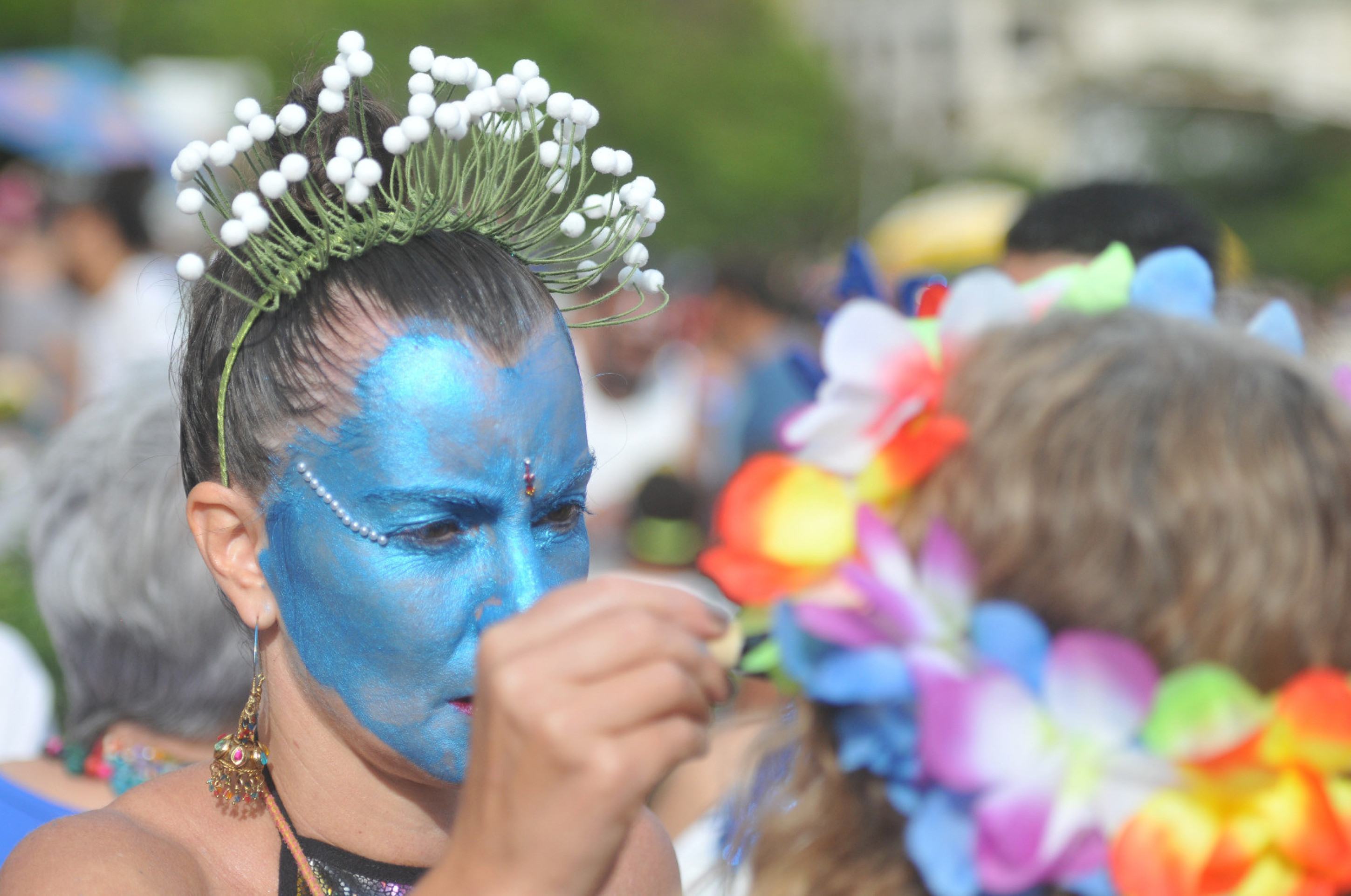 Folião do bloco Pena de Pavão de Krishna, com o rosto pintado de azul, pinta o rosto de outro folião durante desfile do grupo em BH