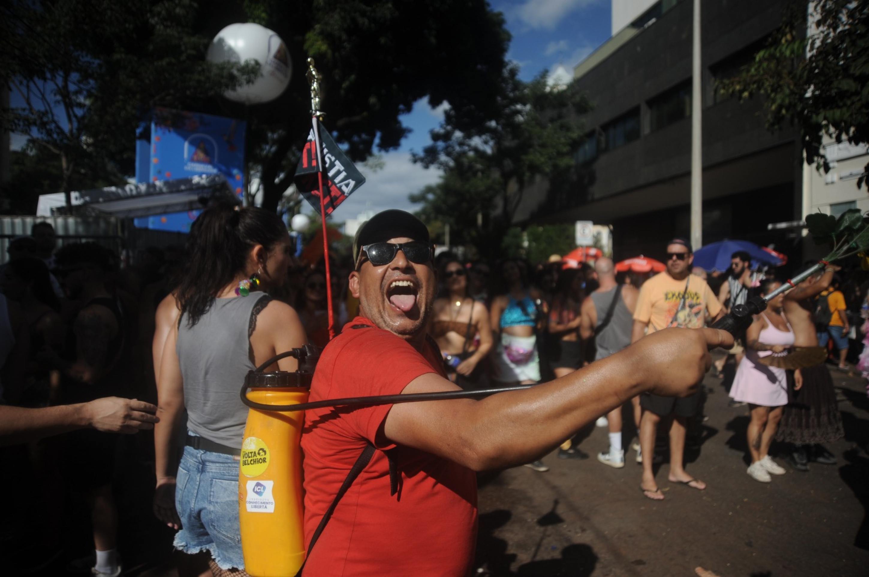 Homem leva pulverizador cheio de água para atenuar calor que atinge foliões durante o bloco Alcova Libertina