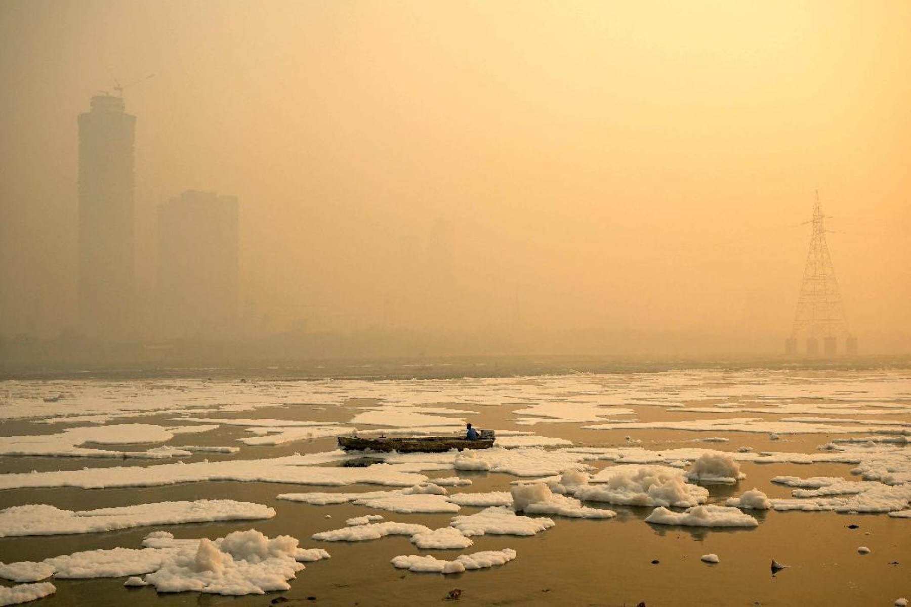 Um homem conduz seu barco pelo Rio Yamuna carregado de espuma tóxica