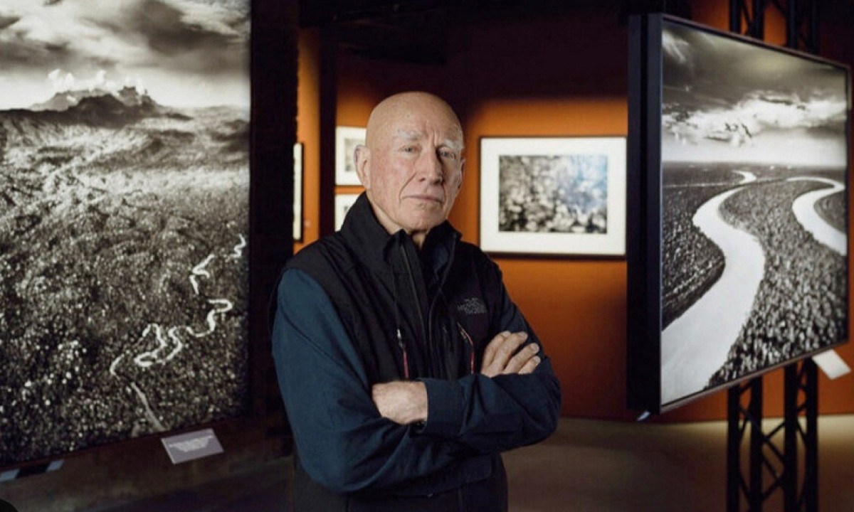 Sebastião Salgado, de braços cruzados, em frente a suas fotos em exposição realizada na França
