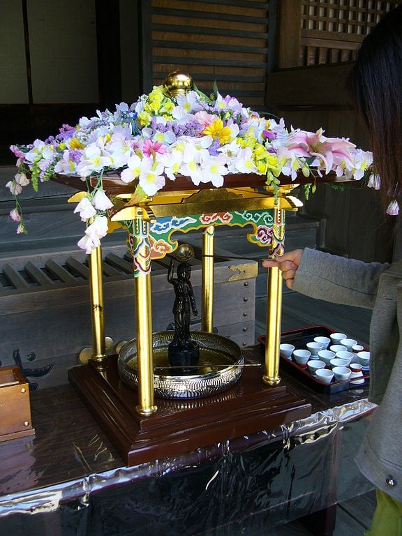 Uma das tradições é banhar os bebês recém-nascidos com chá de hortênsias, no hanamido decorado com flores. Uma estátua de Buda aponta o céu com uma das mãos e a terra com a outra. -katorisi wikimedia commons 