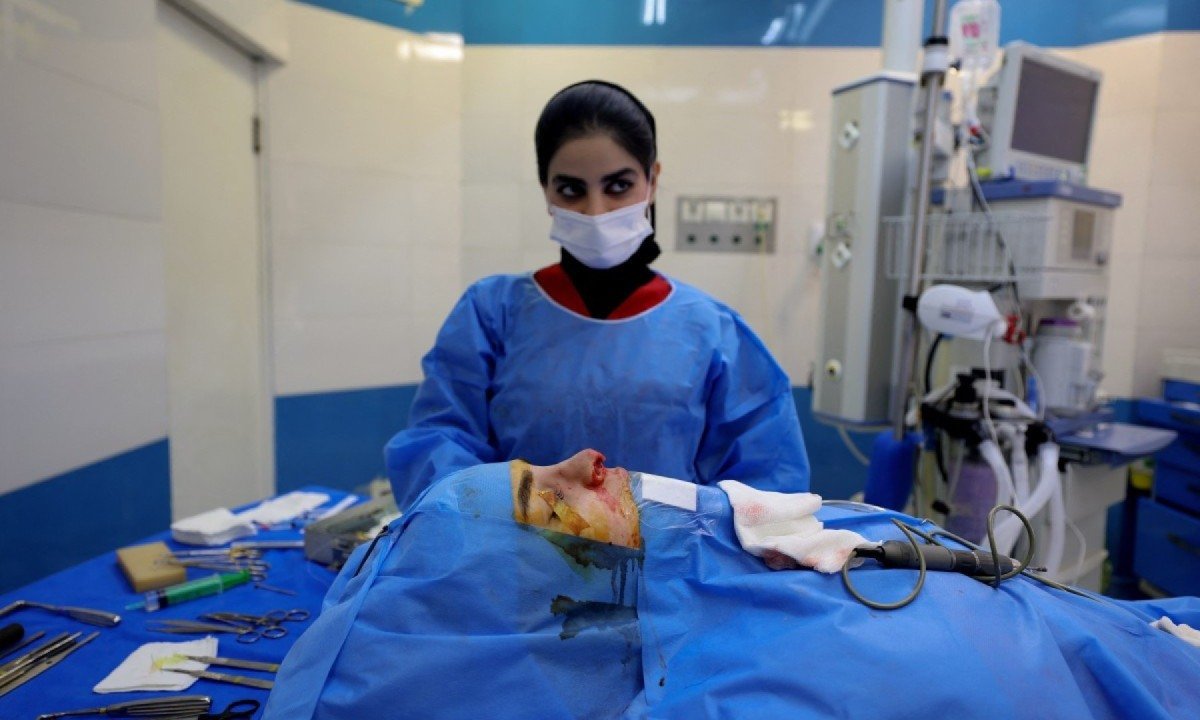 Membro da equipe cirúrgica ao lado de um paciente durante cirurgia de nariz em clínica particular em Teerã, capital do Irã, em 4 de março de 2025 -  (crédito: ATTA KENARE / AFP)