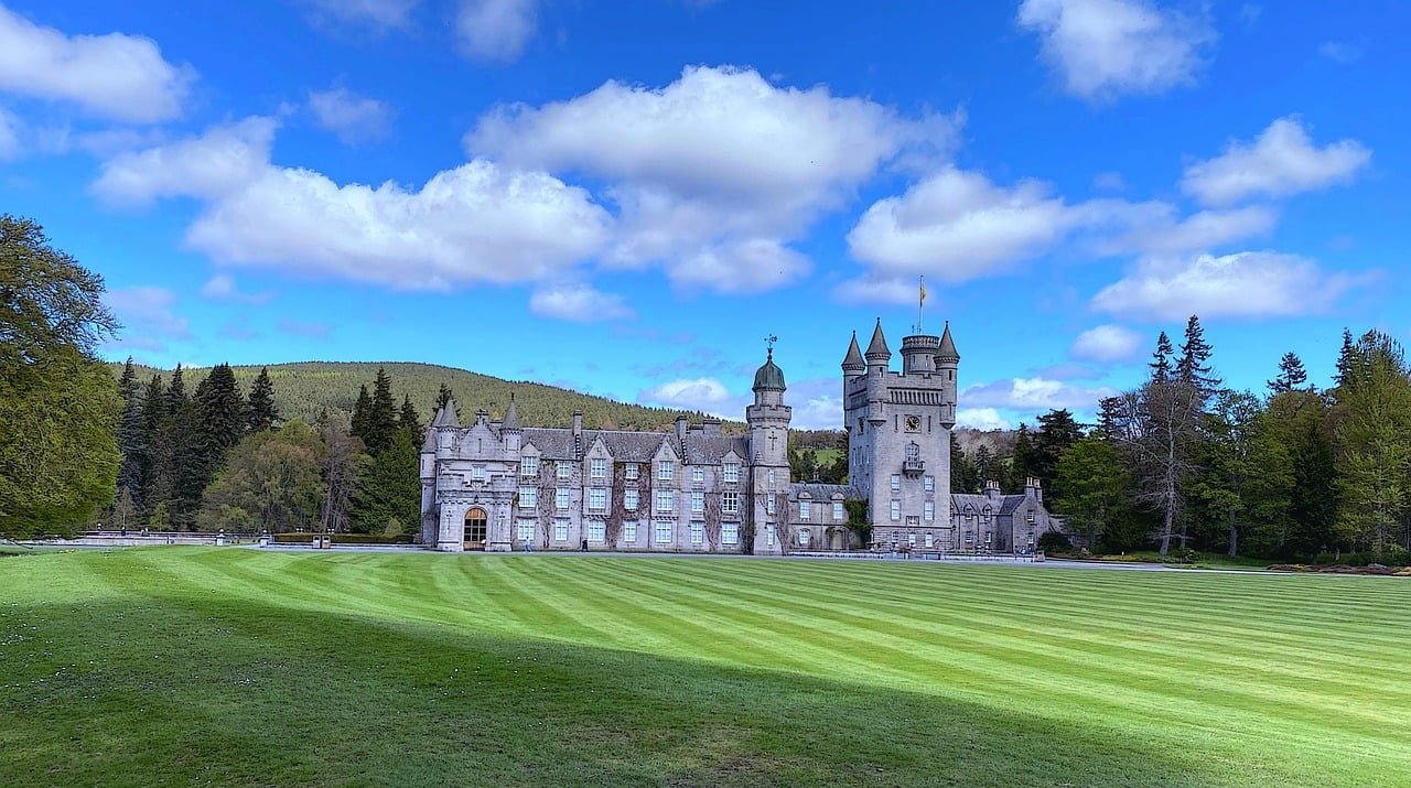 Os jardins do Castelo de Balmoral são vastos, com paisagens exuberantes, árvores antigas, lagos e canteiros de flores bem cuidados. A área ao redor é montanhosa, com florestas, rios e vastas terras abertas que fazem parte da propriedade real.