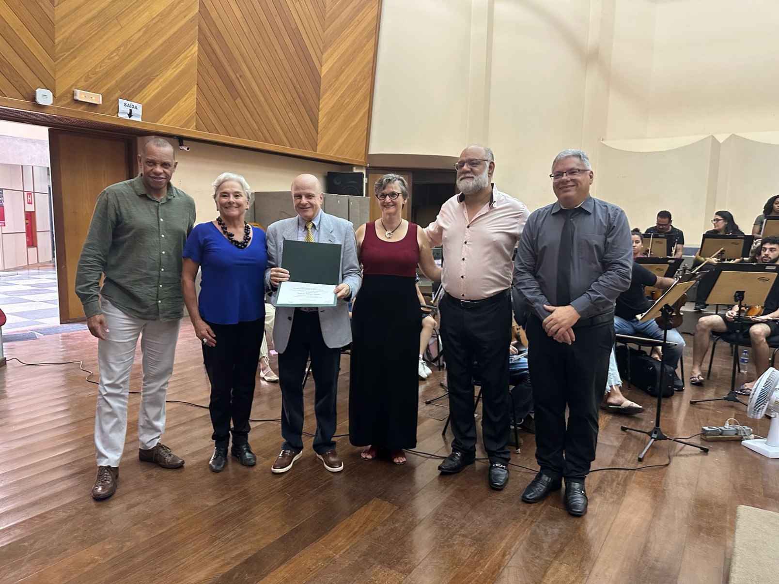Carlos Aleixo, vice-diretor da Escola de Música da UFMG, e Cláudia Malta, diretora artística da Fundação Clóvis Salgado, com o maestro Roberto Tibiriçá, que segura um diploma, Iara Fricke Matte, Mauro Chantal e Charles Roussin, professores da UFMG