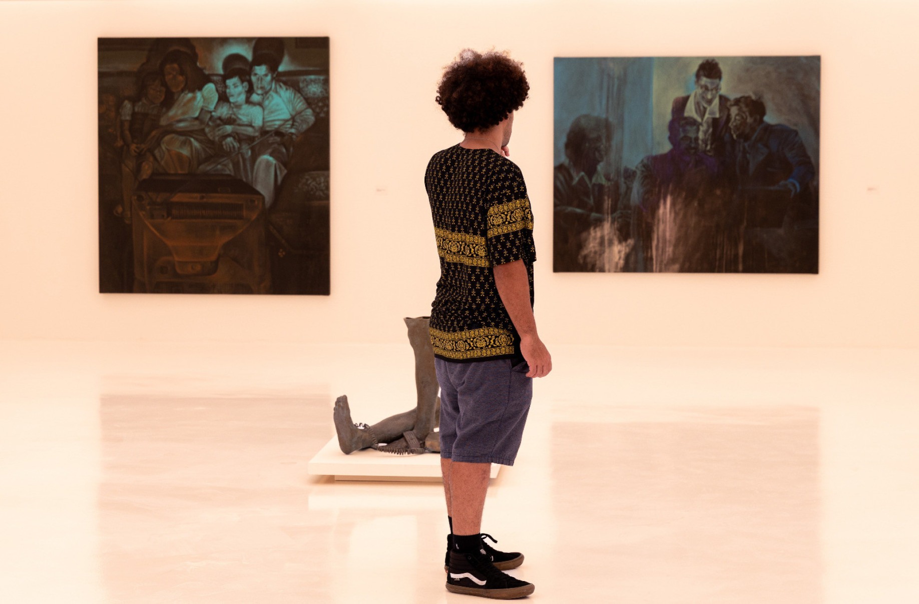 Jovem de bermudas está de perfil e olha para trabalhos do artista plástico Marco Paulo Rolla expostos em galeria de BH