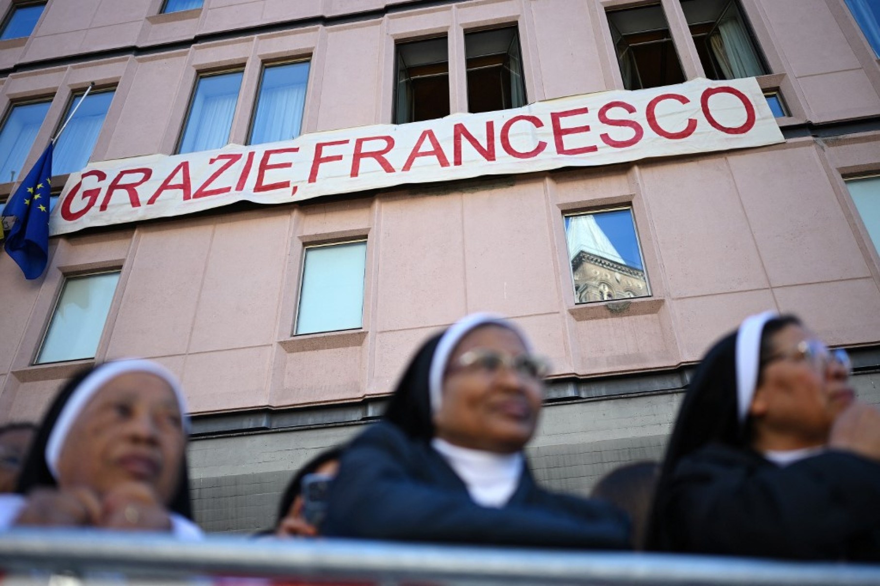 Freiras esperam sob uma faixa com a inscrição em italiano 