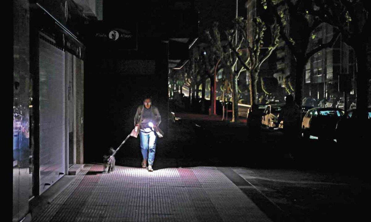 Mulher usa lanterna do celular enquanto passeia com o cachorro em  rua  em completa escuridão na Espanha -  (crédito: MIGUEL RIOPA / AFP)