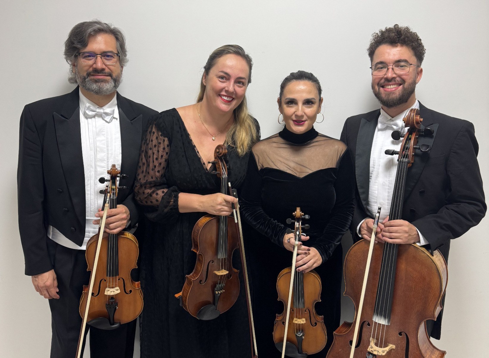 Integrantes do Quarteto de Cordas Catarse seguram instrumentos musicais e sorriem para a câmera