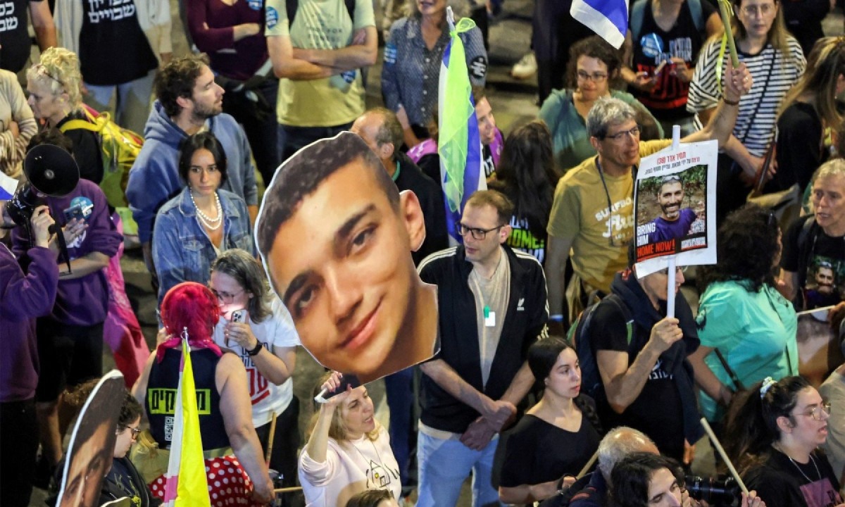 Manifestante segura uma placa com o rosto do refém israelense-americano Edan Alexander (C) durante um protesto pedindo ações para libertar os reféns restantes mantidos em cativeiro em Gaza 
       -  (crédito: Jack GUEZ / AFP)