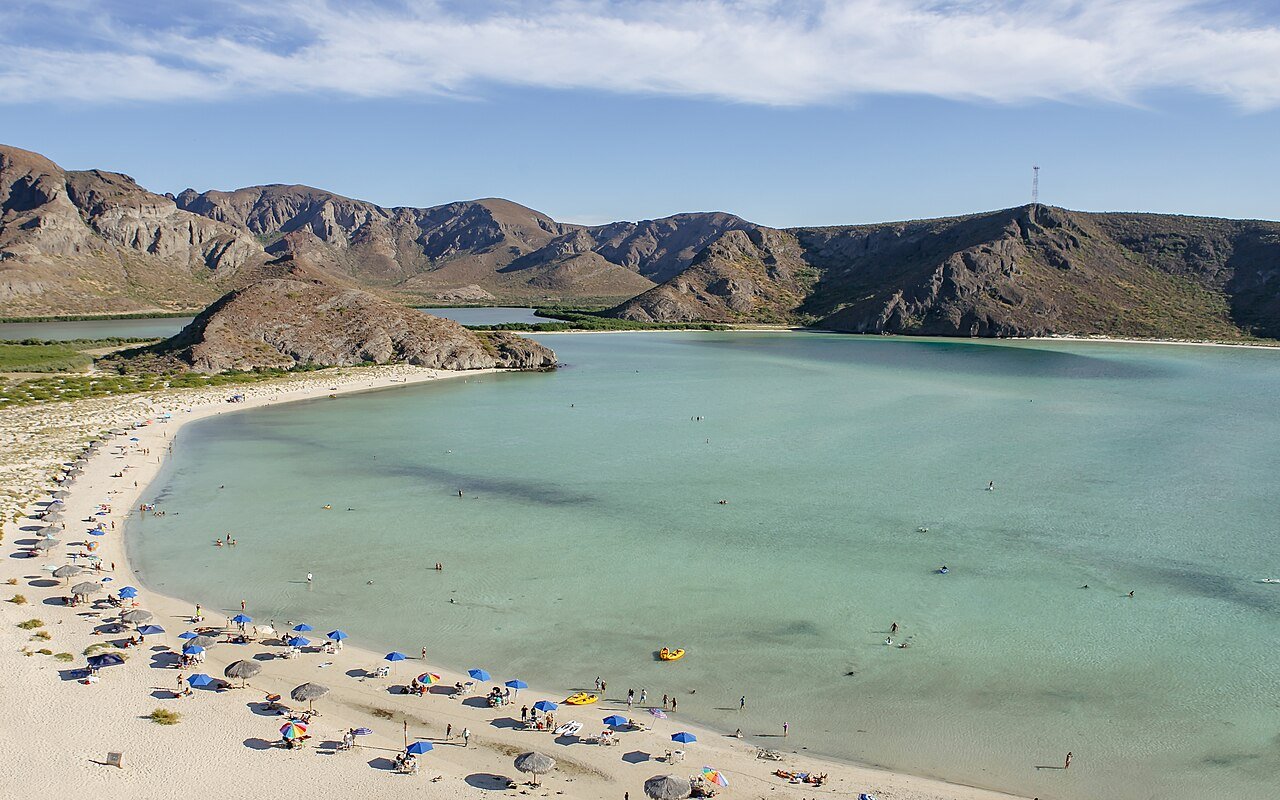 9) Playa Balandra (La Paz, Baja California Sur, México): A praia é conhecida pelas suas águas cristalinas de tons verde-turquesa e azul-celeste, areia branca fina e macia, e um entorno de formações rochosas e muitos cactos.