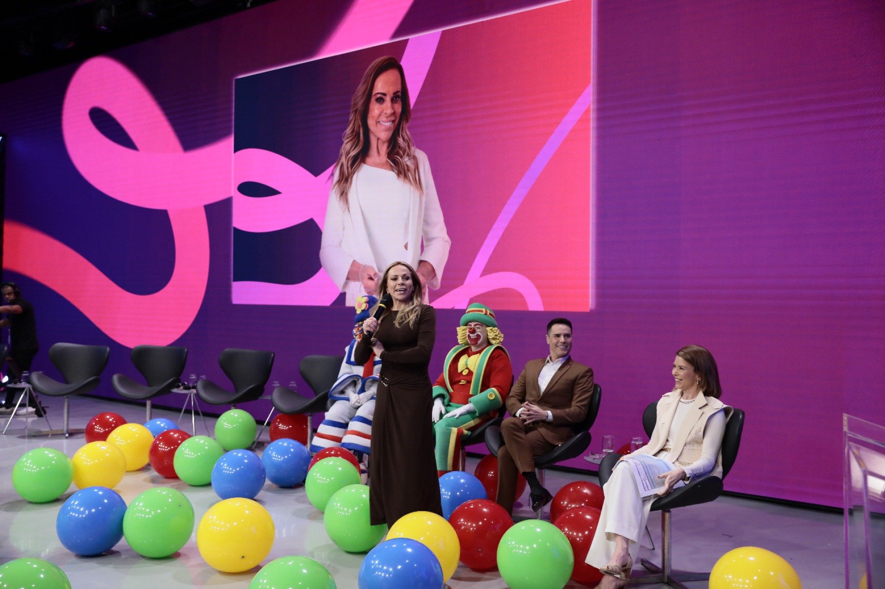 Apresentadora Christina Rocha está em pé, com microfone na mão, falando sobre sua volta ao programa Casos de família