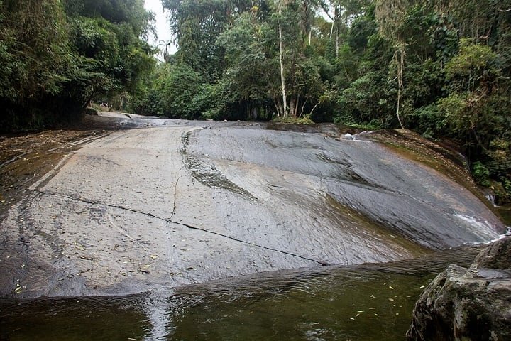O acesso por estrada sinuosa revela vistas espetaculares, e a região também oferece trilhas, como a que leva à Cachoeira do Tobogã, onde é possível deslizar por uma rocha natural.