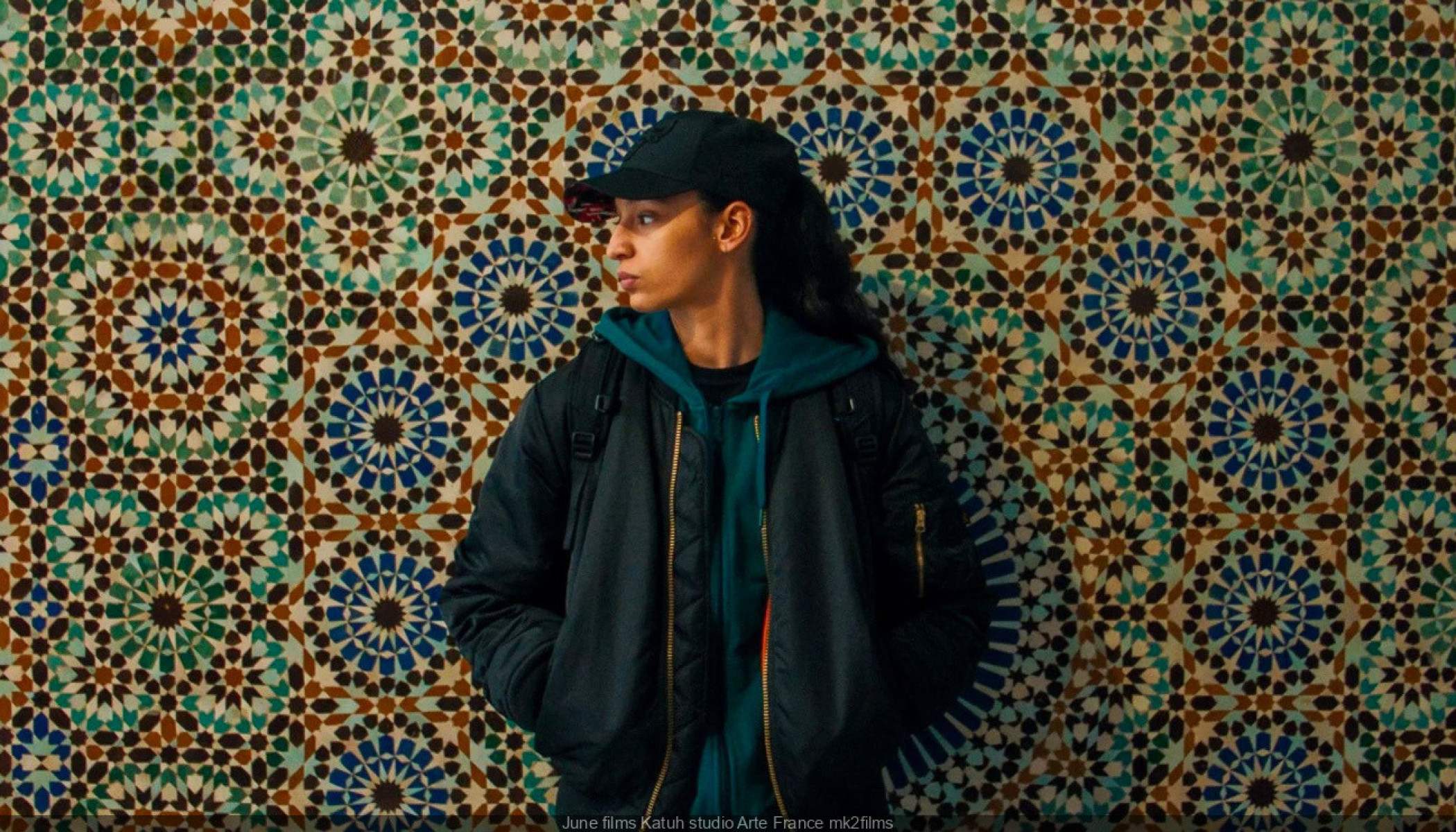 Atriz Nadia Melliti usa boné e está de lado, encostada em parede de azulejos em cena do longa 'The little sister', da diretora Hafsia Herzi 