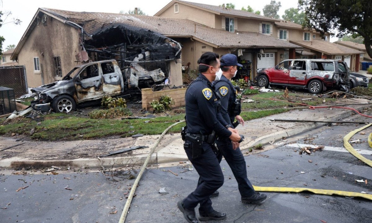 Policiais fazem buscas no local da queda do avião em uma rua residencial de San Diego, na Califórnia
      -  (crédito: Sandy Huffaker / AFP)
