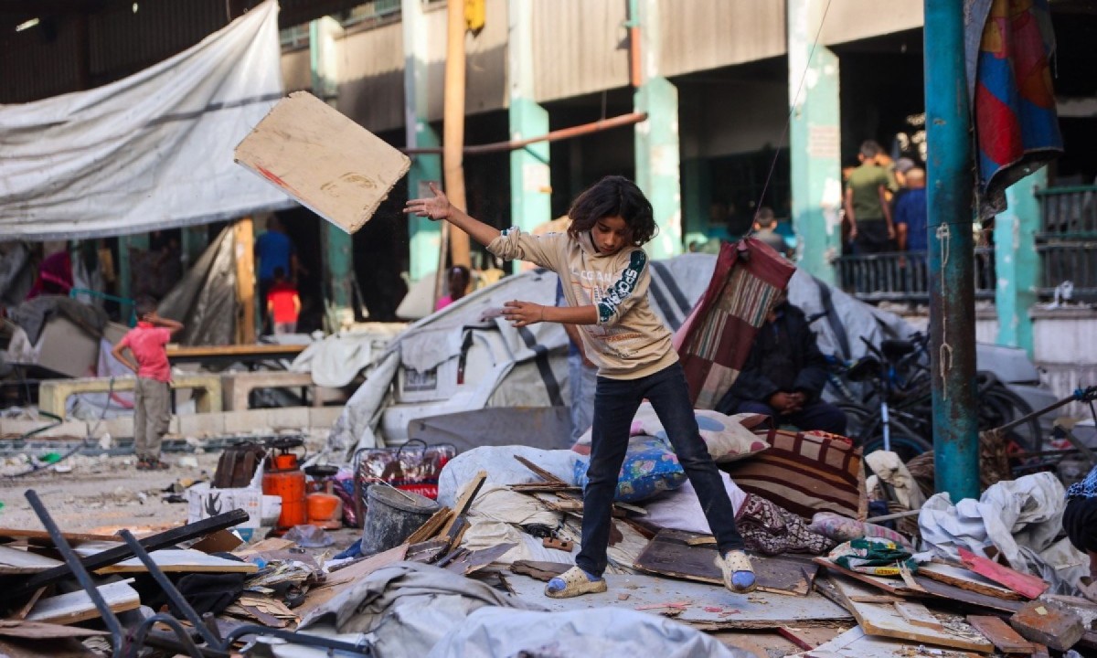 Menino separa seus pertences em meio aos escombros da Escola Fahmi Al-Jarjawi, na Cidade de Gaza, em 26 de maio de 2025, após um ataque israelense -  (crédito: Omar AL-QATTAA / AFP)