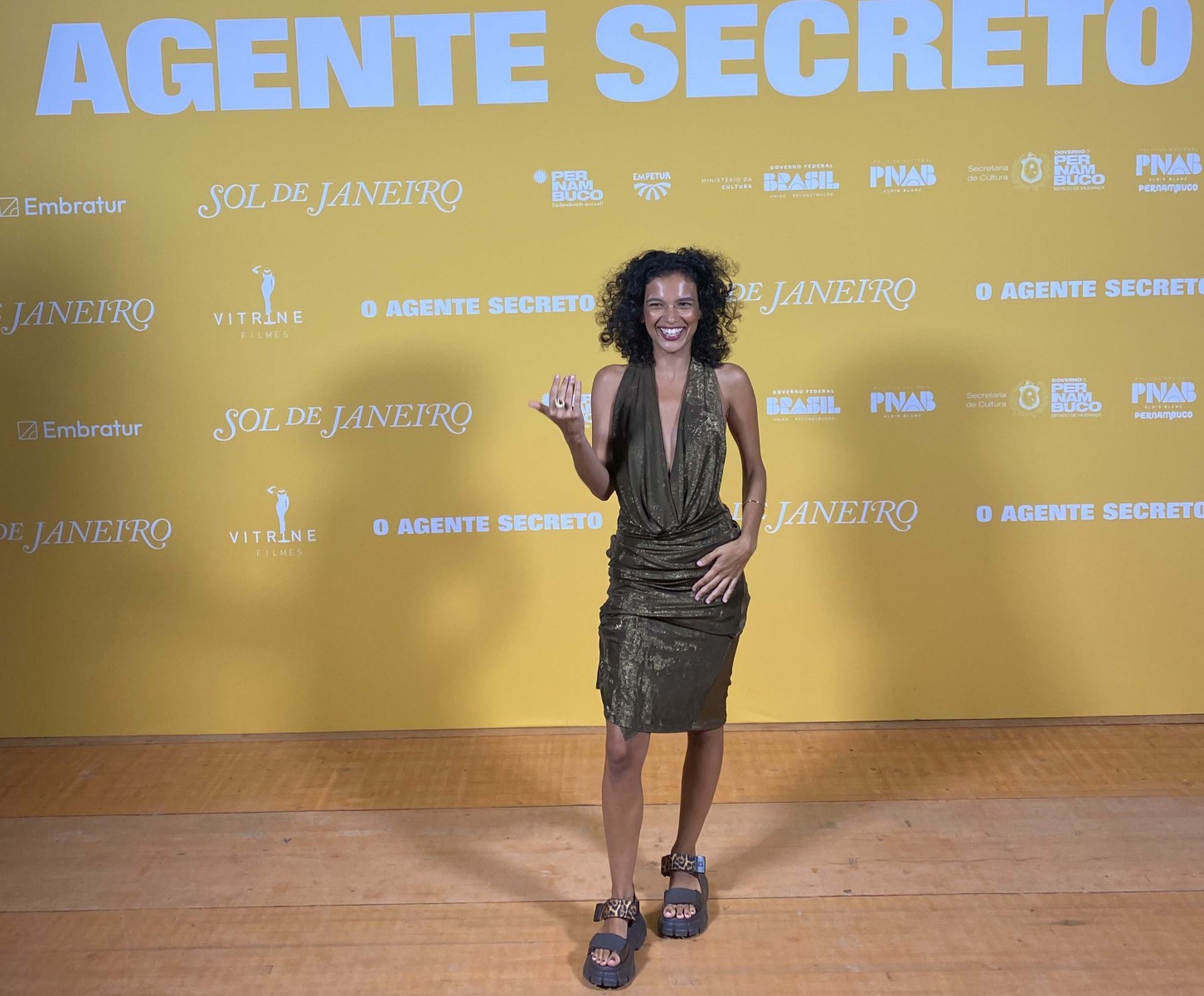 Atriz Laura Lufési posa à frente de painel do filme O agente secreto