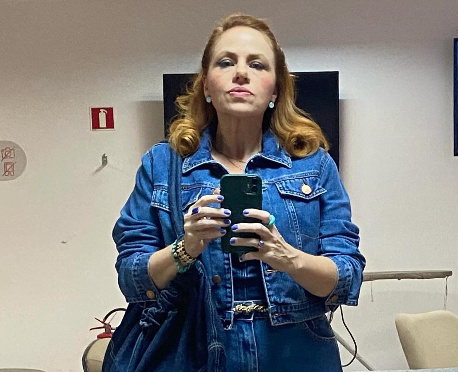 Karine Teles veste roupa azul e tem unhas pintadas de azul, como a secretária Aldeíde da novela Vale tudo
