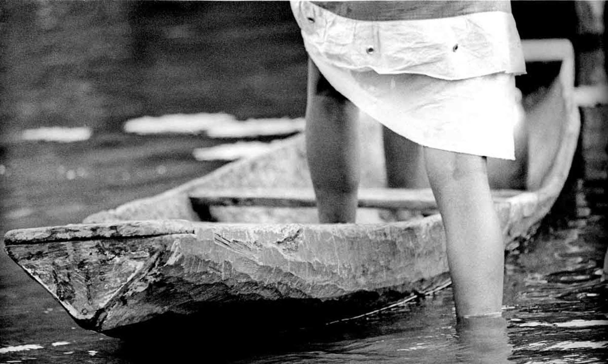 Foto em preto e branco mostra canelas e saia erguida de mulher prestes a subir em barco no Pará 