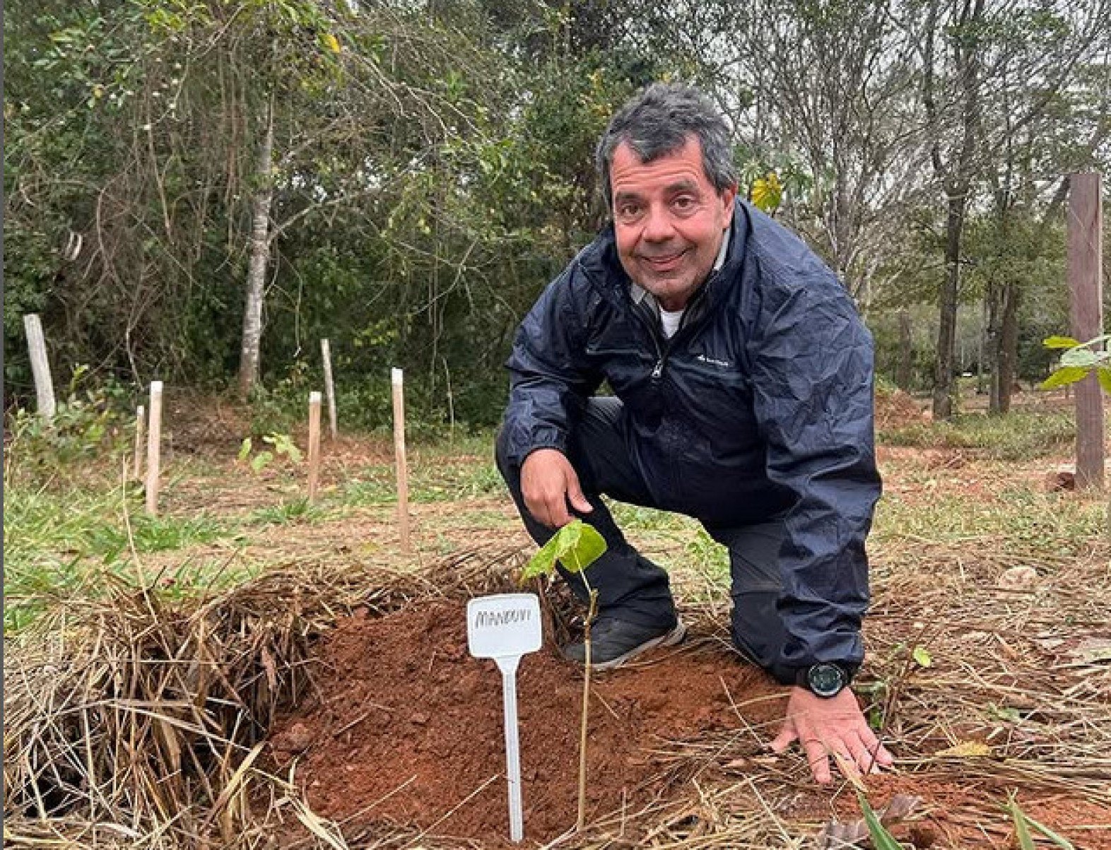 Fotógrafo Mário Barila posa atrás de placa indicando o plantio de muda