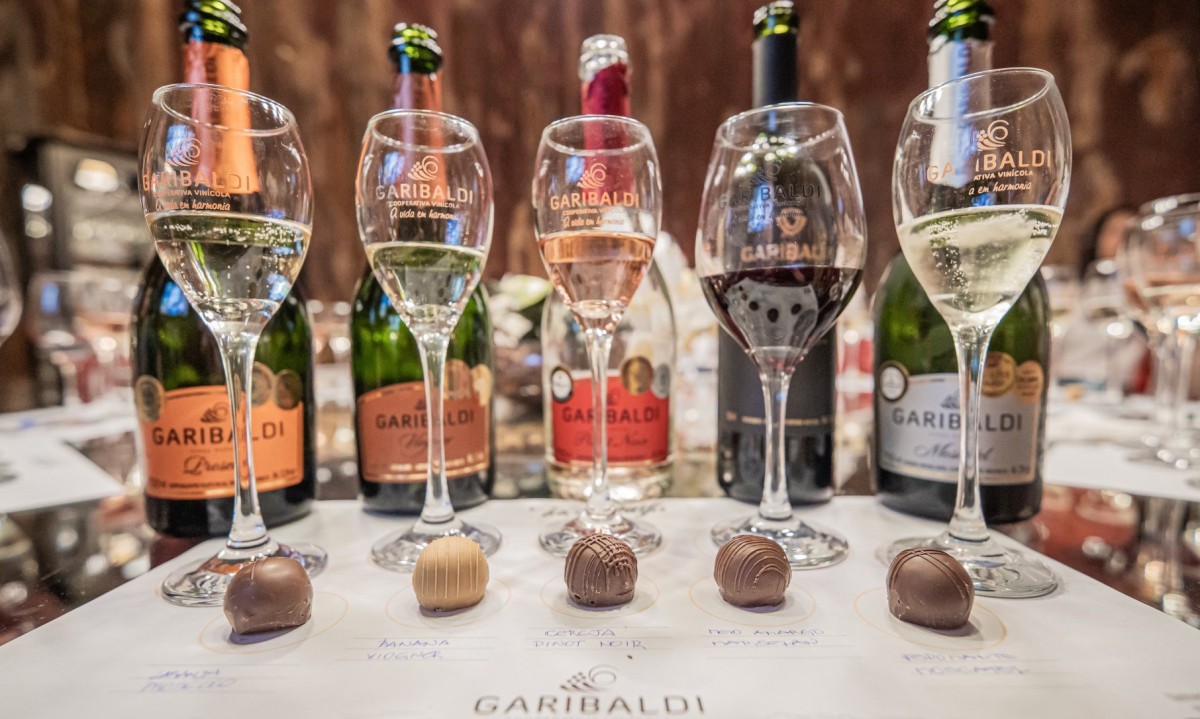 Garrafas de espumantes alinhadas com taças e trufas em mesa da Cooperativa Vinícola Garibaldi