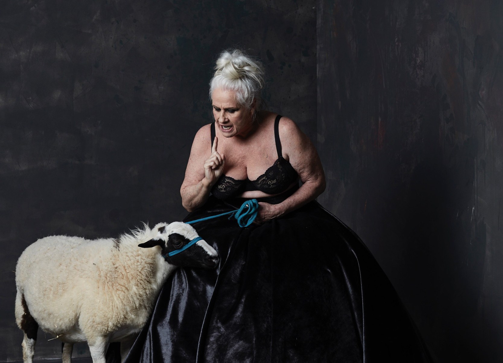 Vera Holtz usa vestido de baile preto e conversa com um carneiro em cena da peça Ficções 