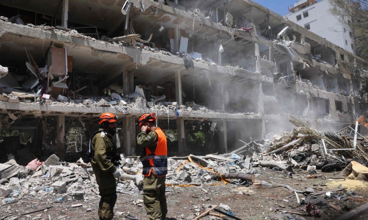 Forças de segurança israelenses observam enquanto uma escavadeira limpa os escombros de um prédio destruído no local de um ataque iraniano que atingiu um bairro residencial na área de Ramat Aviv, em Tel Aviv. Pelo menos 16 pessoas ficaram feridas e pelo menos um impacto foi relatado no centro de Israel depois que o Irã lançou duas ondas de mísseis no país após o bombardeio dos EUA em suas instalações nucleares, disseram serviços de resgate e relatórios -  (crédito: Jack GUEZ / AFP)