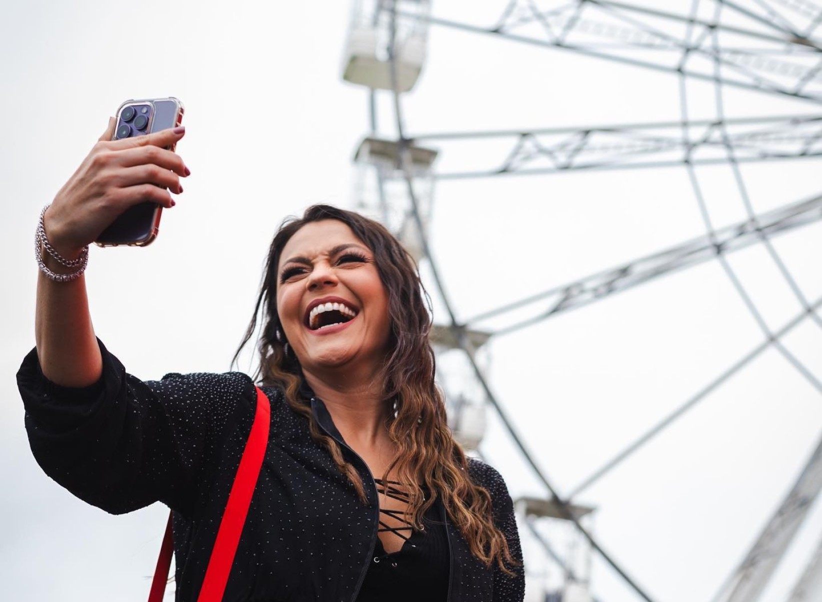 Bruna Louise faz selfie sorrindo em frente a roda gigante