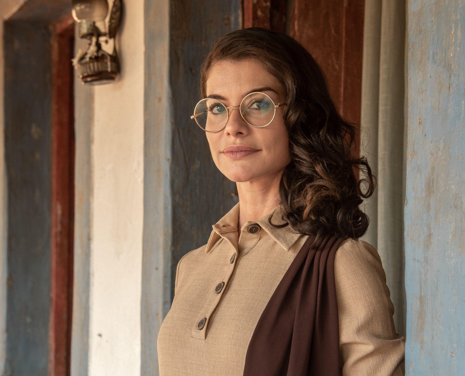 Usando óculos e roupa bege, a atriz Alinne Moraes está caracterizada como Jânia, personagem da novela Guerreiros do Sol