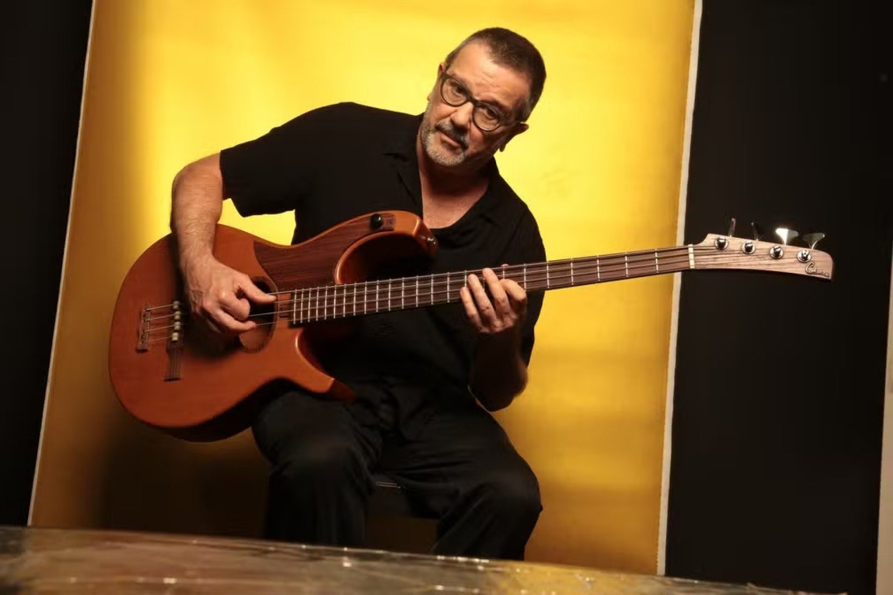 Músico Rodolfo Stroeter está sentado tocando baixo