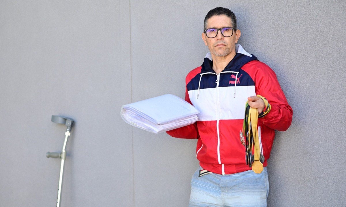 Em uma m&atilde;o, ele diz carregar sua vit&oacute;rias, que s&atilde;o suas medalhas e o livro escrito por ele e, na outra, o calhama&ccedil;o de documentos m&eacute;dicos, que seriam suas derrotas -  (crédito: Leandro Couri/EM/DA Press)