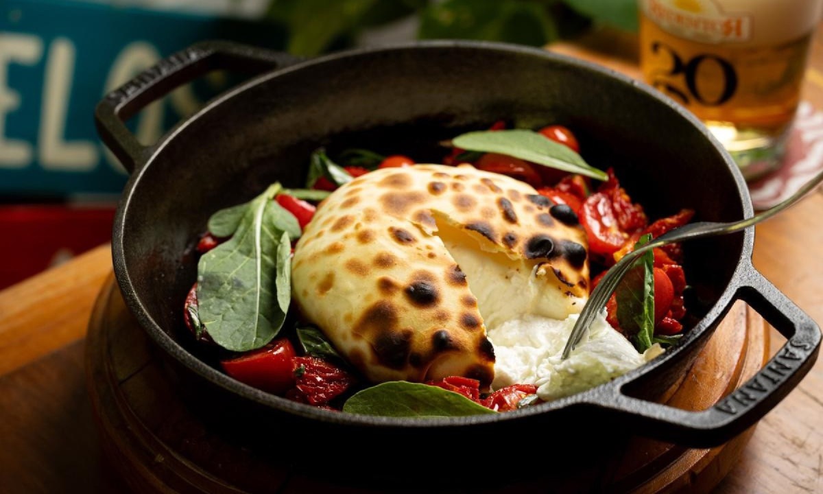 Burrata servida com duetos de tomates confitados, molho pesto e rúcula