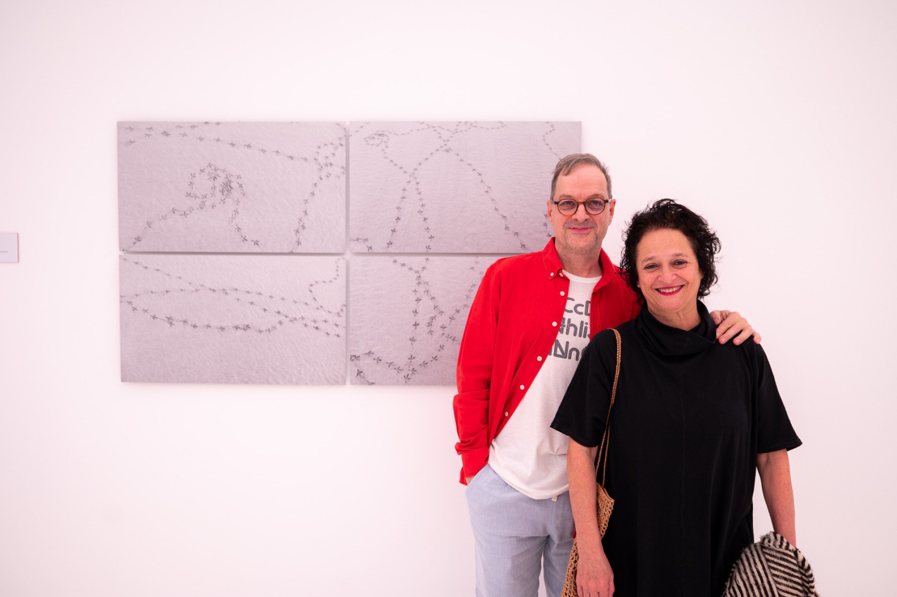 Marcelo Drummond e Nydia Negromonte sorriem para a câmera e têm atrá de si uma obra do artista plástico Cao Guimarães