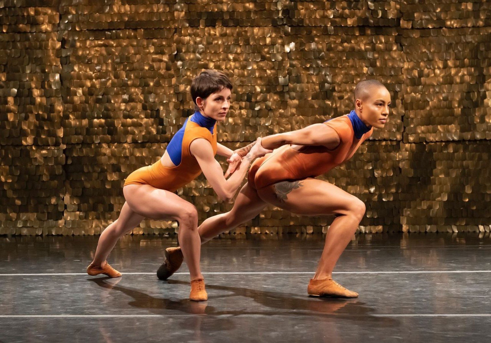 Dois bailarinos estão agachados, lado a lado, em coreografia de Piracema, espetáculo do Grupo Corpo