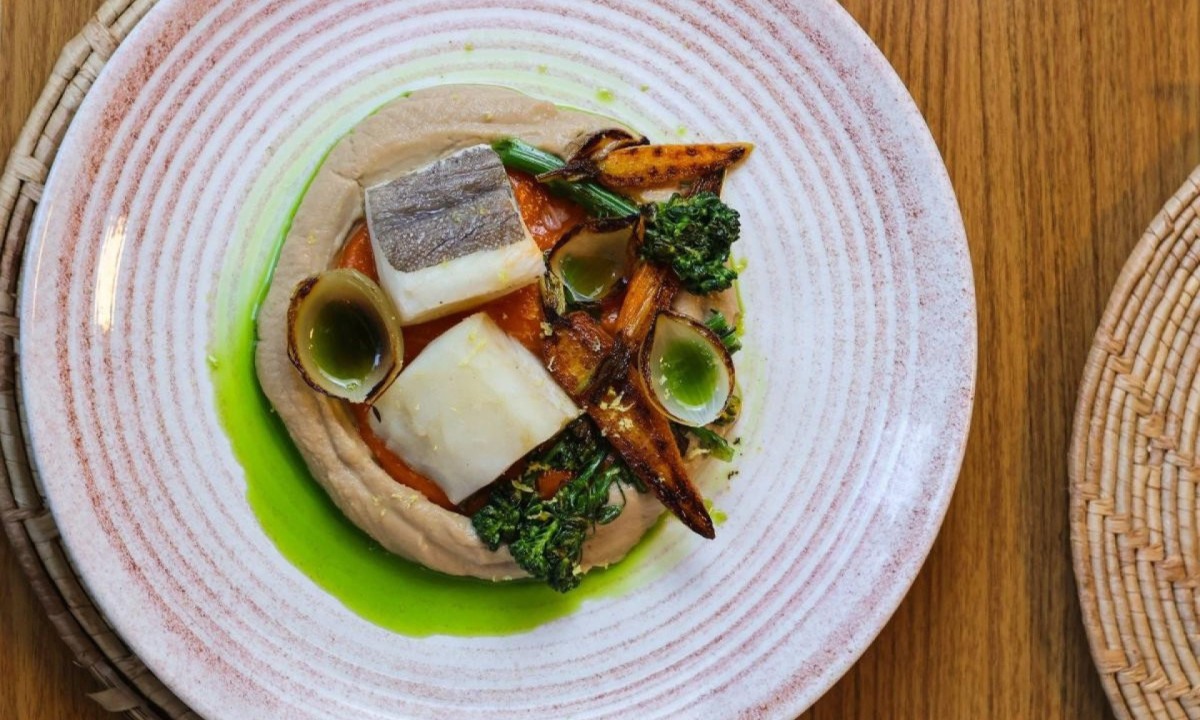 Na foto, Bacalhau da Noruega confitado, servido sobre um delicado creme de couve-flor caramelizada, acompanhado de vegetais tostados e finalizado com molho romesco