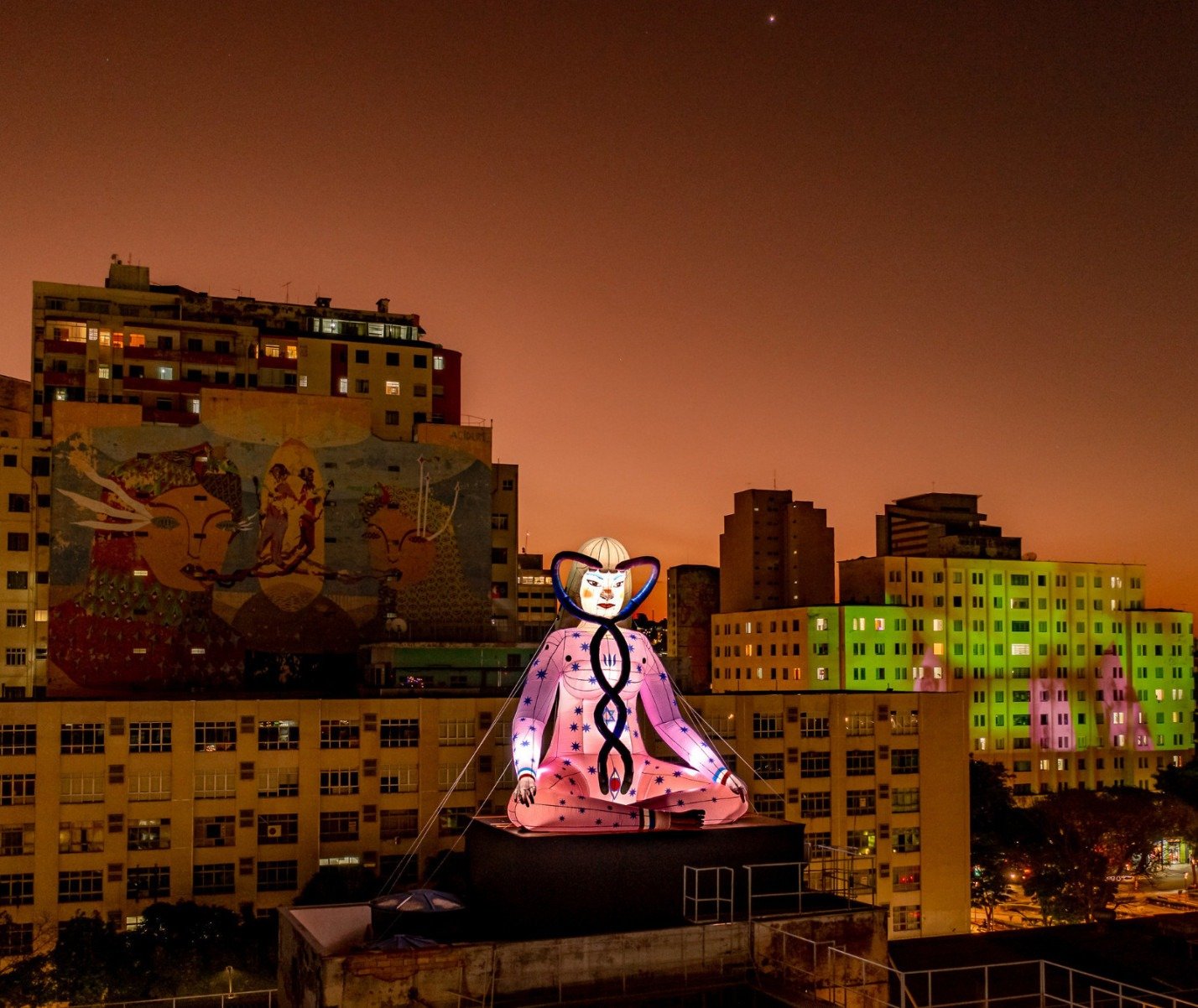  Instalação de figura iluminada, sentada como Buda, em cima de prédios na região da Praça da Estação, em BH