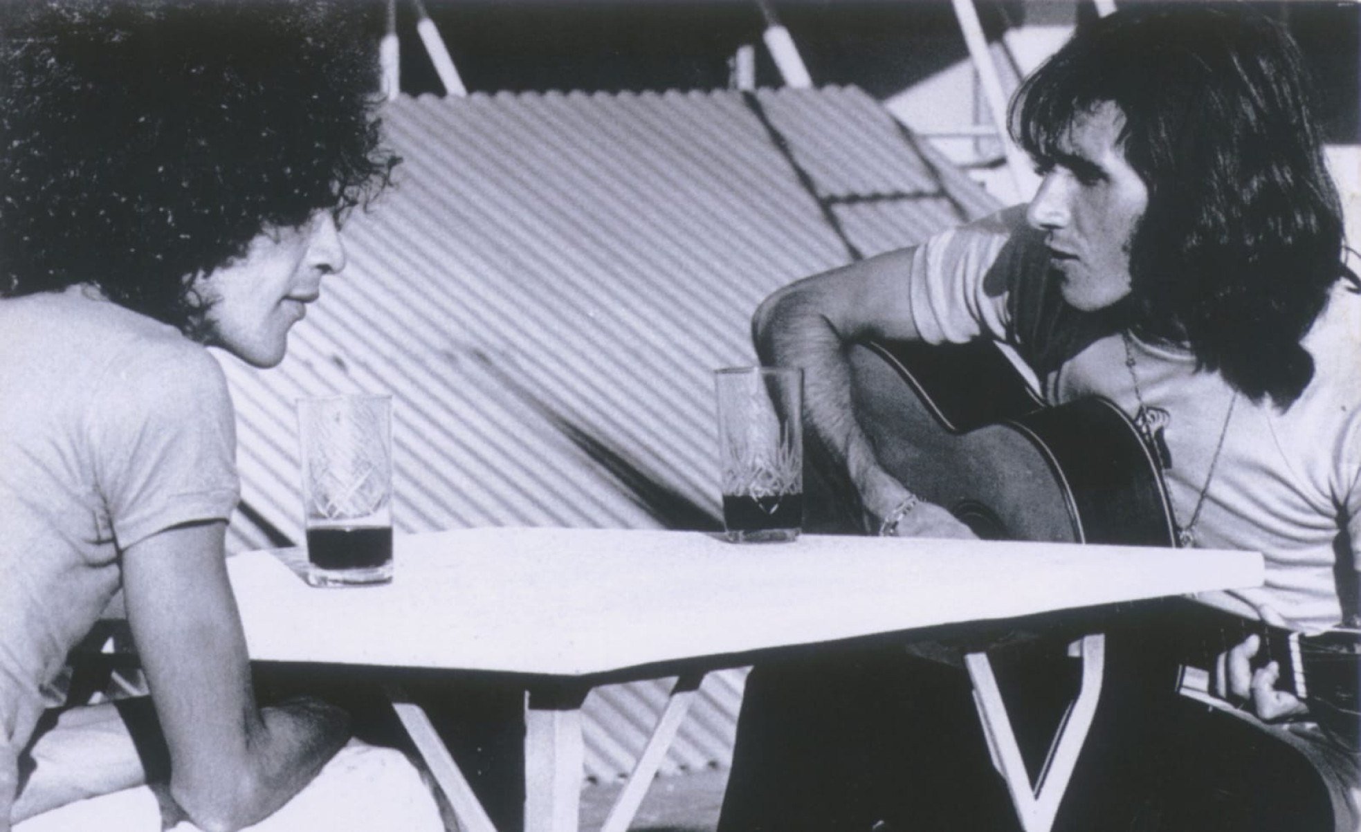 Caetano Veloso e Odair José sentados à mesa, cantando. Odair toca violão