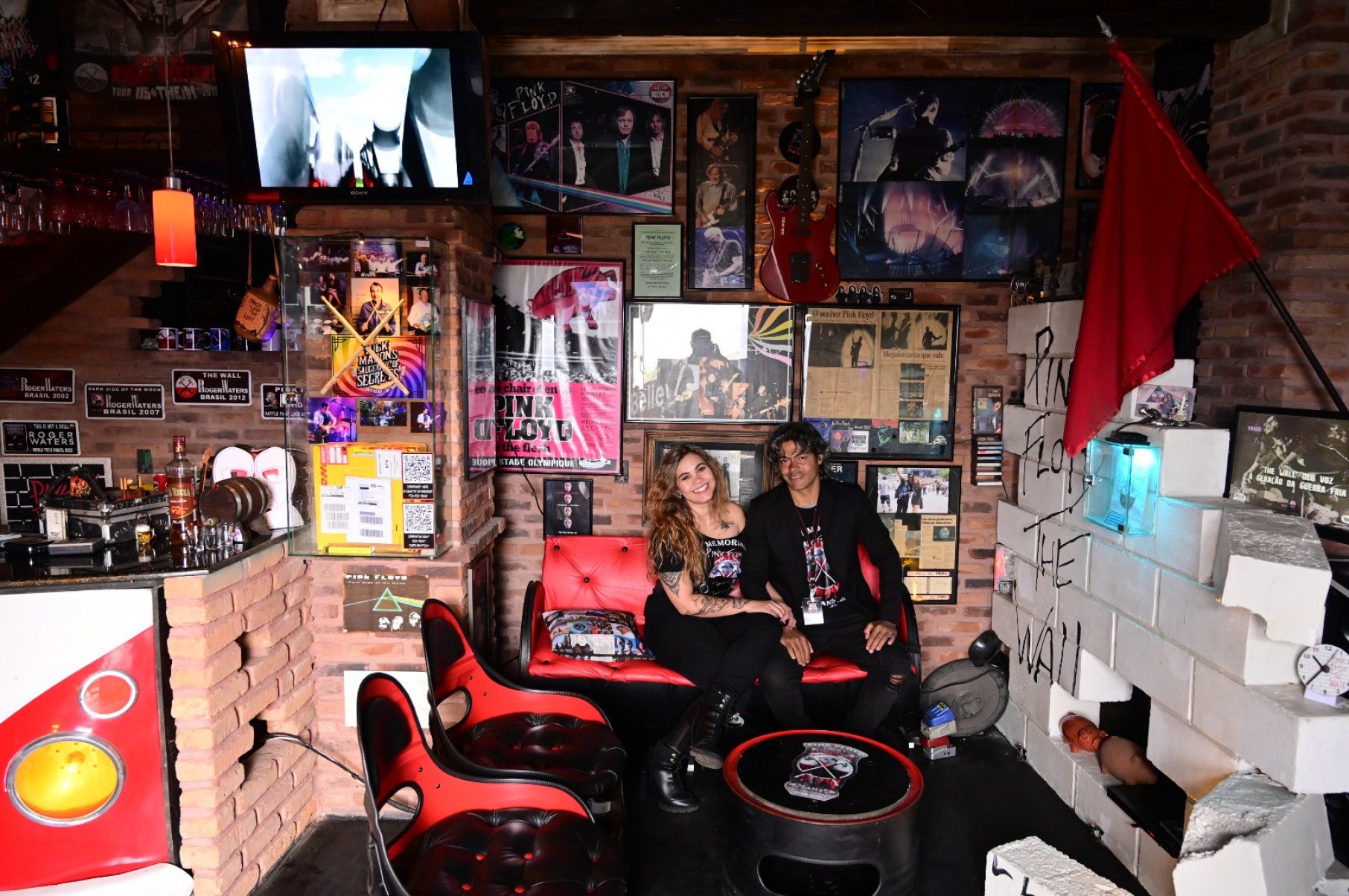 Wesley Cristiano de Souza e a mulher, Mikaelly, sentados em sala do  Memorial Pink Floyd Fans, sorriem para a câmera