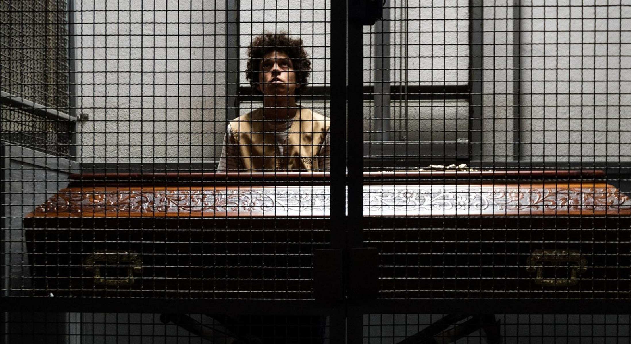 Ator João Nunes Monteiro está atrás de uma grade e tem caixão de defunto diante de si no filme Sonhar com leões