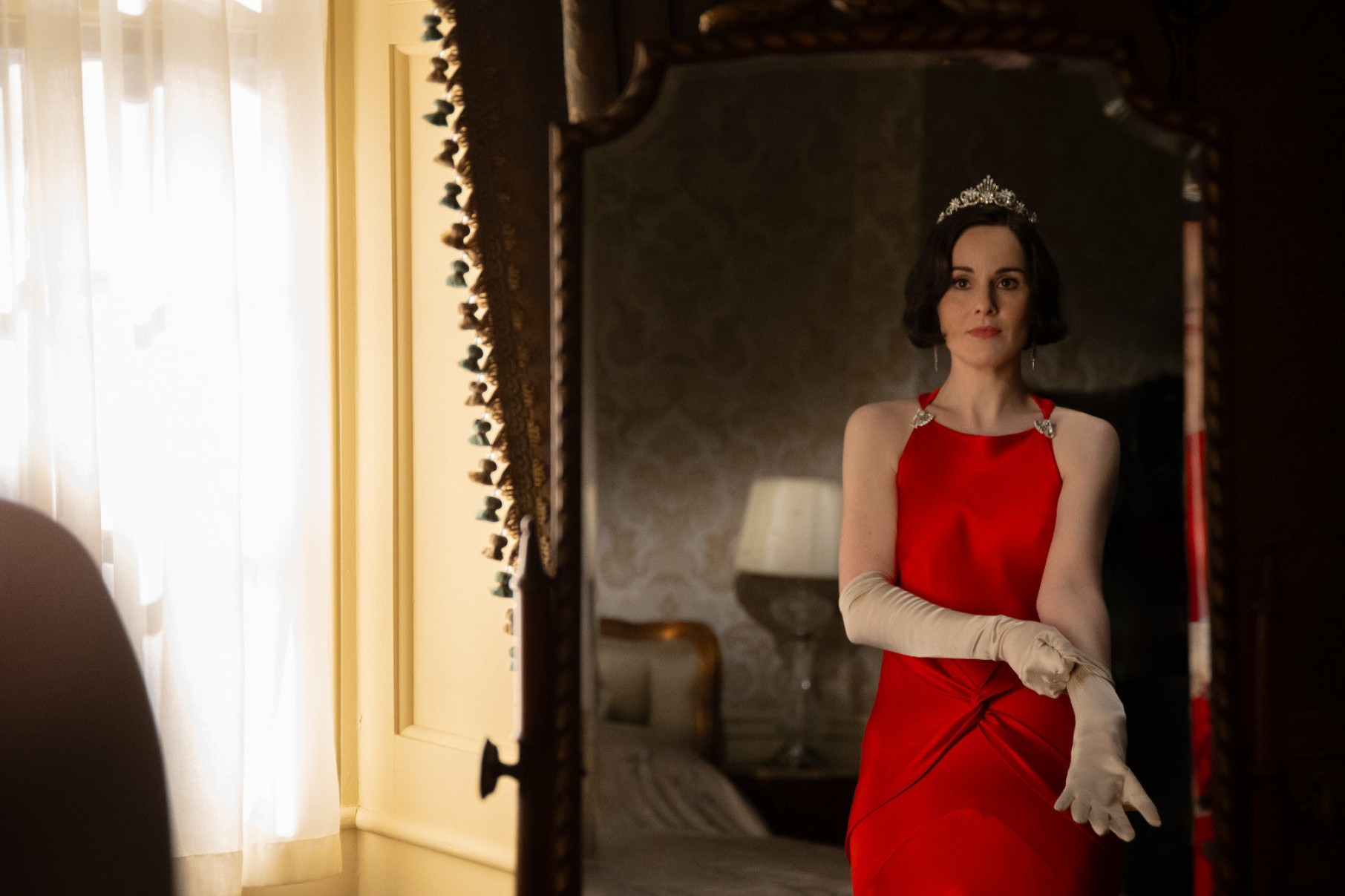 Atriz Michelle Dockery, com vestido de baile vermelho, se olha no espelho