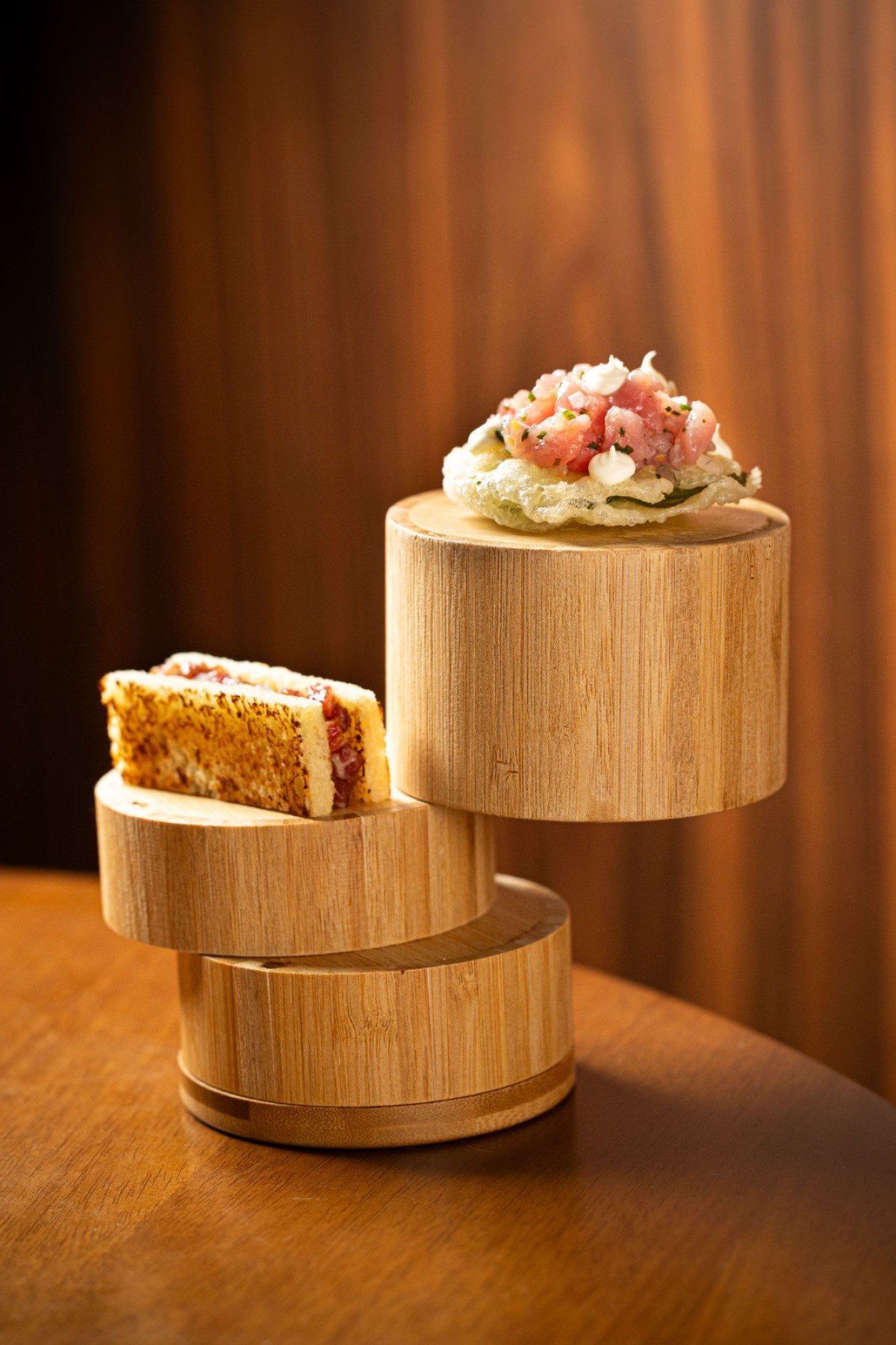 Sanduíche de brioche amanteigado com tartare de angus ao lado de tempurá de capuchinha com crudo de atum e sour cream defumado