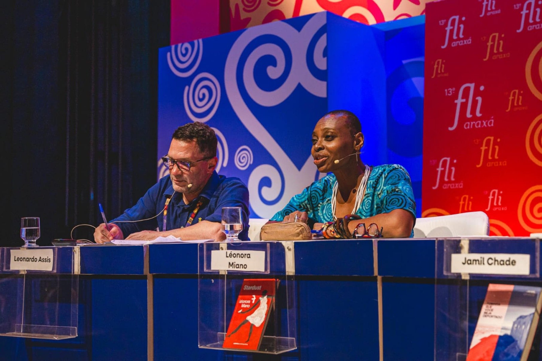 Mesa-redonda de evento com homem branco e mulher negra, com cabeça raspada
