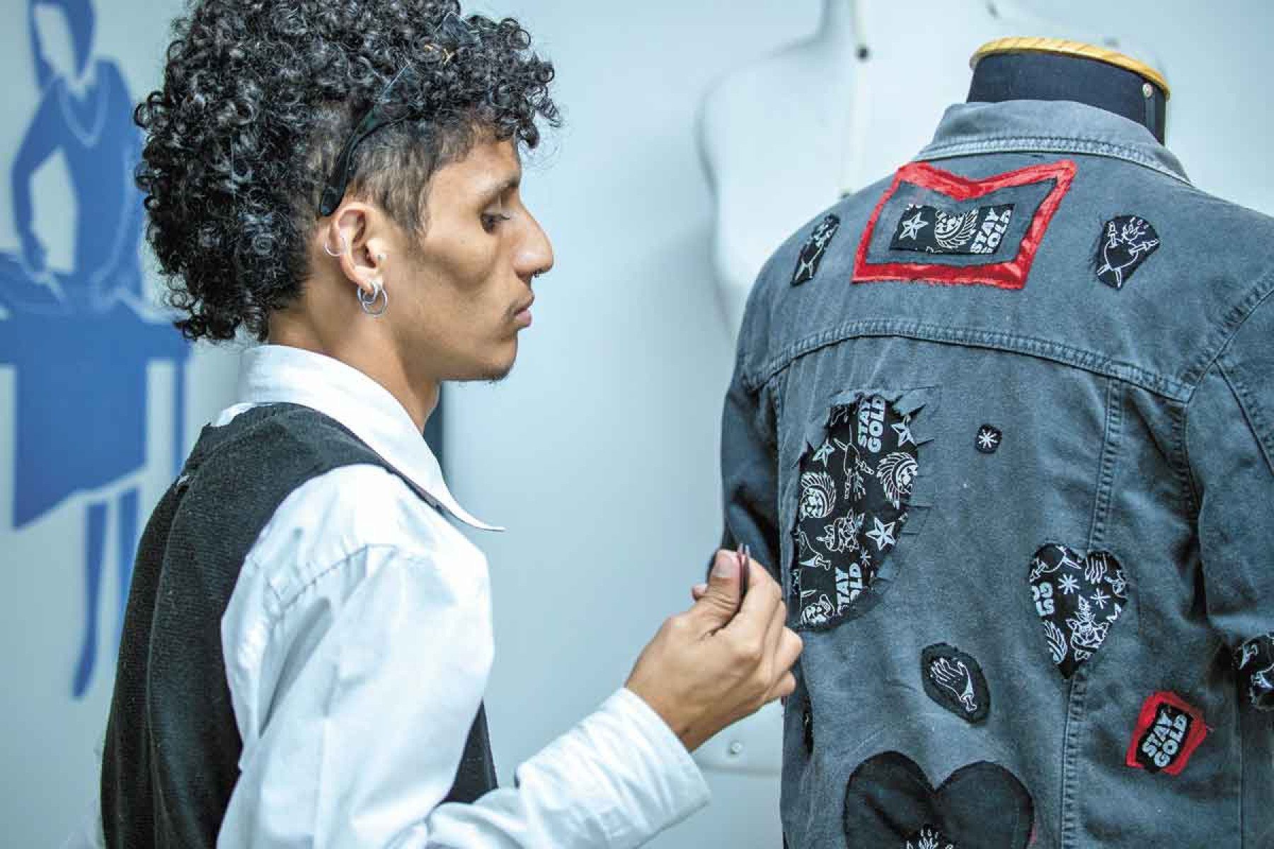 Rapaz está de lado, retocando roupa em manequim 